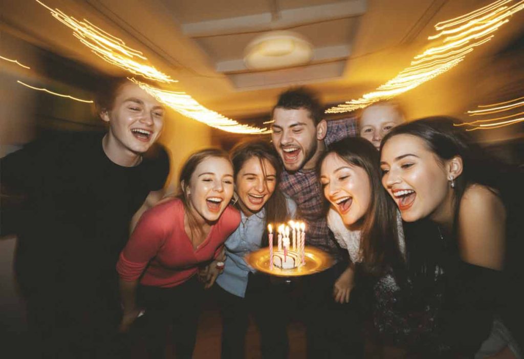 A dynamic birthday moment captured mid-celebration - a blurred group shot with movement, laughter, glowing candles, and fairy lights. The background has natural bokeh and motion blur, conveying energy and joy like a photo dump collage aesthetic.