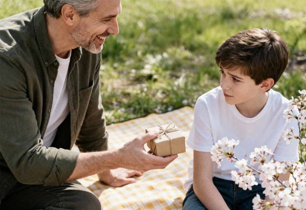 Stepparent offers a small gift to a shy preteen during a bright spring picnic.