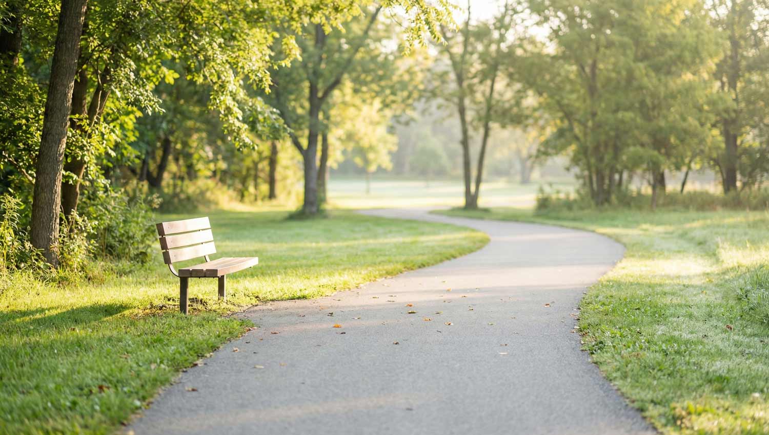 An outdoor scene in early morning or late afternoon: a quiet path, empty bench, or open doorway with light spilling in. No visible people, but strong sense of movement forward. Soft colors, natural elements, subtle depth. The feeling is gentle beginnings, permission, and ease. Photorealistic, minimalist composition.