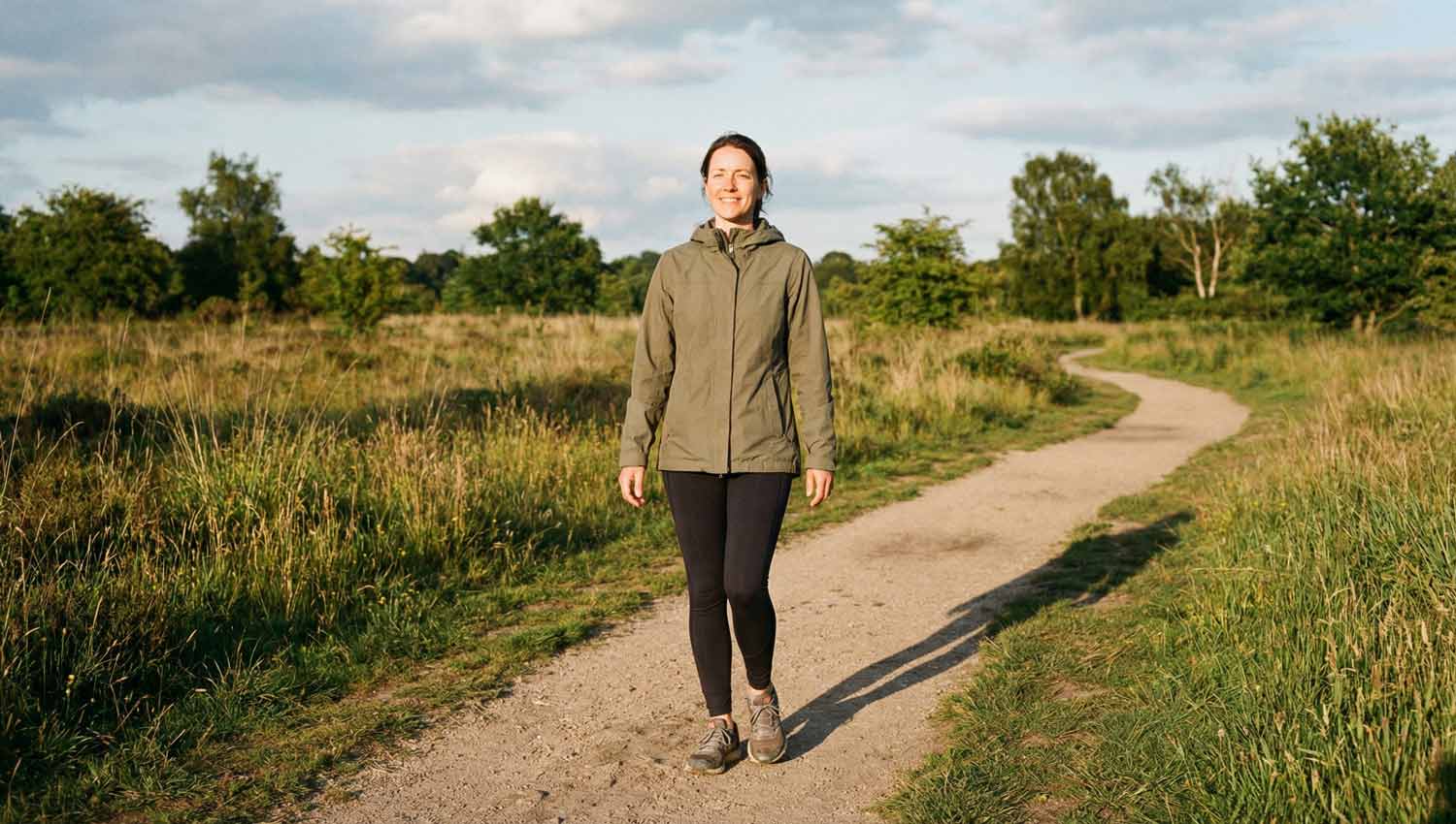A peaceful outdoor moment — a person walking alone on a quiet path, trees or open sky around them. No phone visible, no shopping bags. Clothing is simple and unbranded. Natural light, spacious composition, emphasis on openness and breathing room. Realistic, cinematic but grounded.