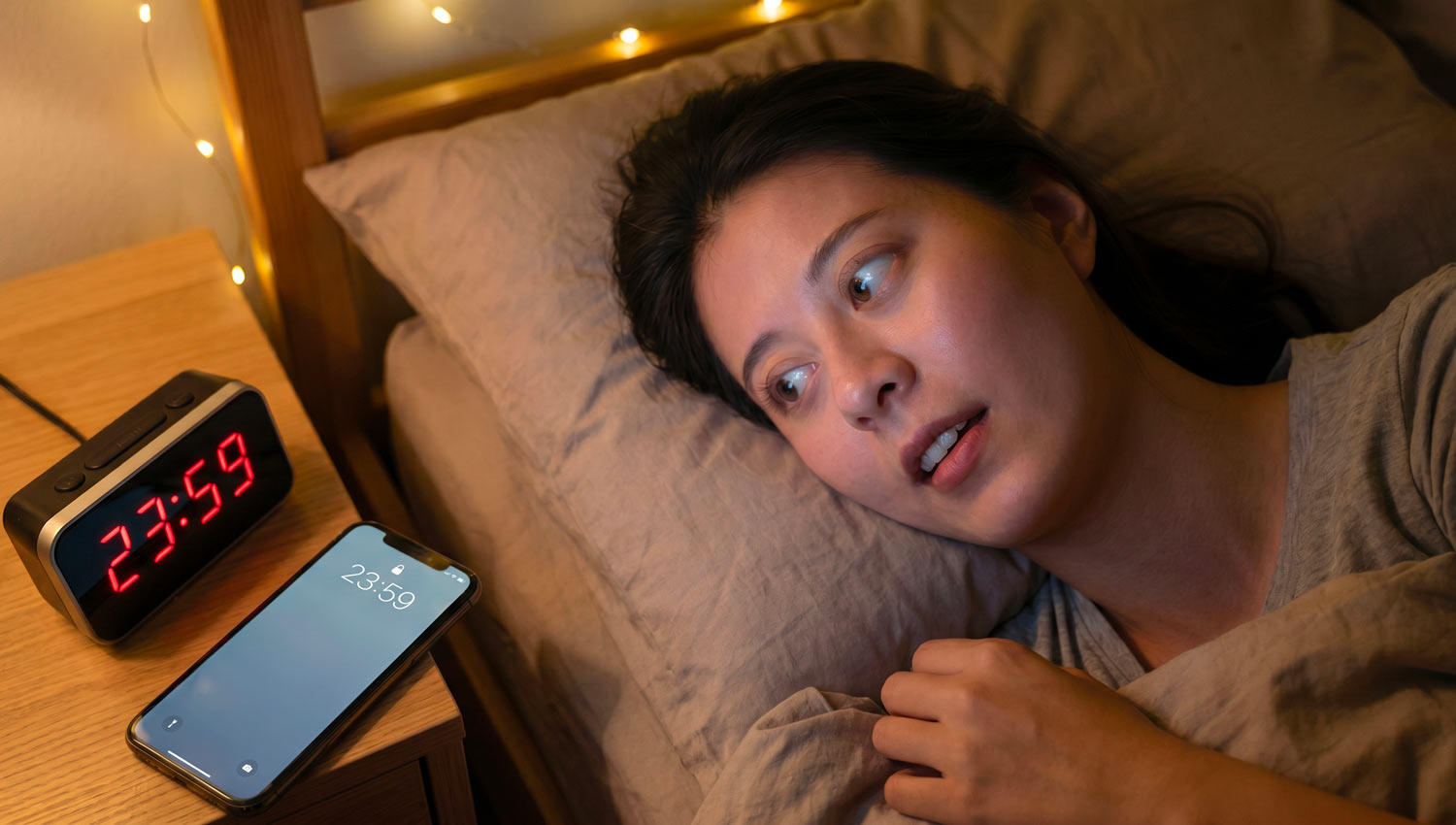 A realistic close-up of a person lying in bed at night, staring at their phone anxiously as the clock hits 11:59 PM turning to 12:00 AM, anticipation visible on their face, dark room with soft ambient light, reflections of the phone screen in their eyes, intimate and emotional mood, ultra-realistic skin texture, low-light photography style