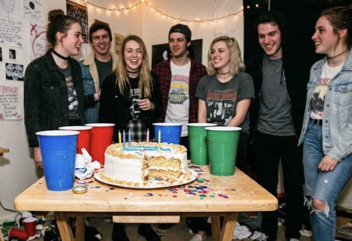 A nostalgic, slightly blurry flash photo of young adults celebrating a birthday in a cozy, decorated bedroom.